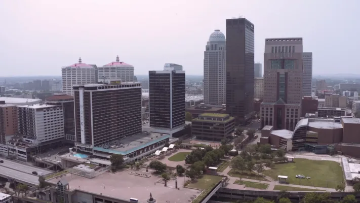 Downtown Louisville skyline featuring modern office towers, hotels, and cultural buildings with green plaza space in foreground