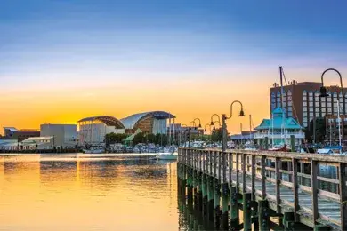 Waterfront boardwalk with amusement park rides and buildings reflected in water at golden hour
