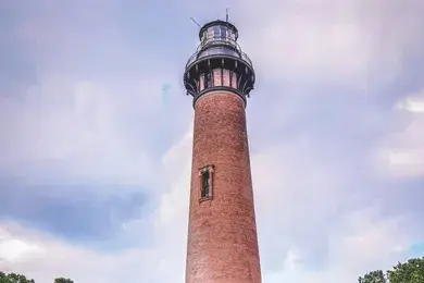 Tall brick lighthouse tower with lantern room at top against cloudy sky